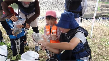 観察ケースに入った魚や生きものを覗き込んで笑顔を見せる子どもたち