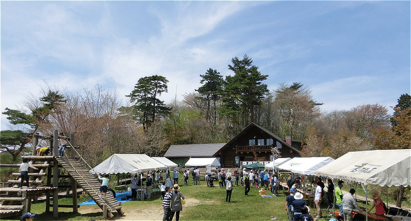 「金剛山 山の秋まつり」の会場風景。澄み切った青空のもと、木造ロッジ前の広場に白いテントが並び賑わう様子