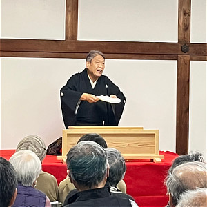 高座で扇子を手に噺を披露する落語家と客席の様子