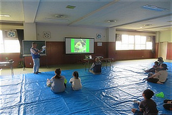 室内でスクリーンを使ってセミの一生について解説を聞く参加者たち