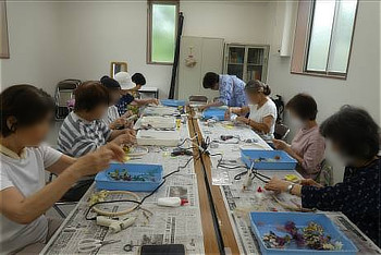 室内で、テーブルを囲んでドライフラワーリースを作る講座の様子。複数の参加者が作業をしている。