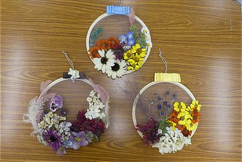 木枠の刺繍枠に、色とりどりのドライフラワーをあしらった完成したリースが3つ並んでいる様子。