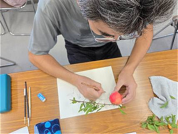 片手でザクロの実を支えながら、真剣な眼差しで紙に下絵を描き進める参加者